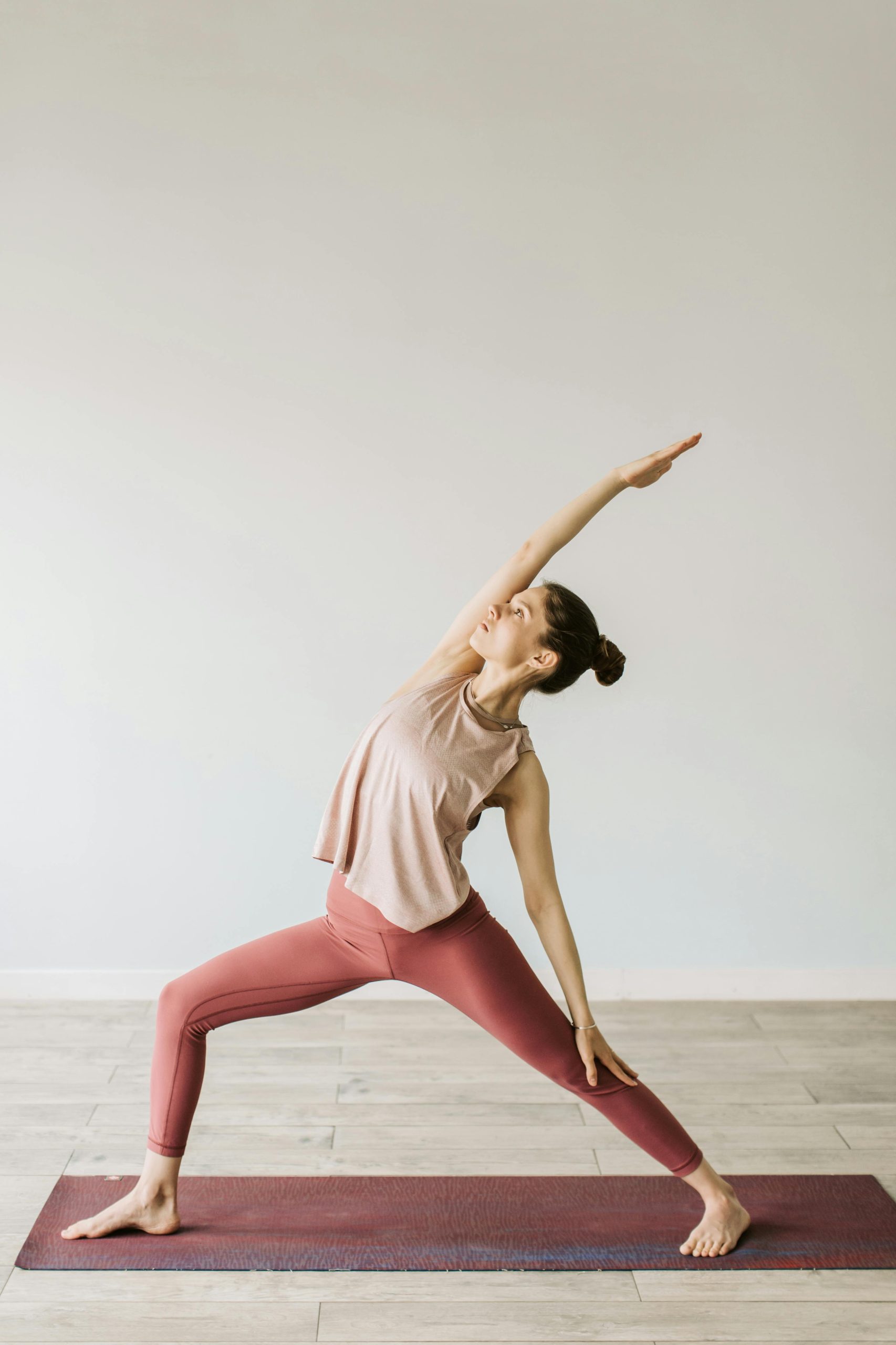 A young woman practices the Warrior yoga pose indoors on a sunny day.