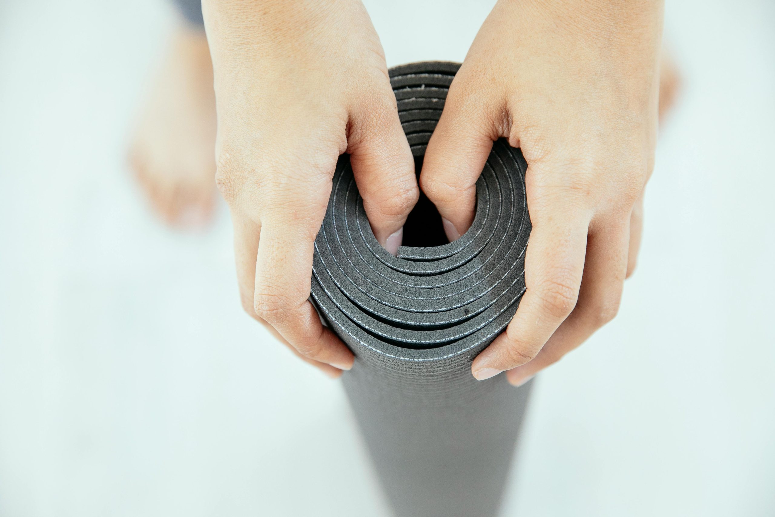 Top view of crop unrecognizable female holding gray rolled yoga mat placed in vertical position